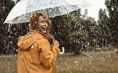 Frau steht mit einer gelben Regenjacke und einem Regenschirm im Regen