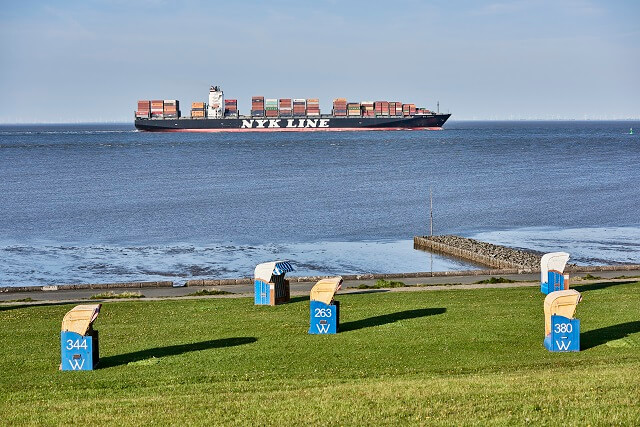 Der Deich und die Grimmershörnbucht mit bunten Strandkörben und einem Containerschiff im Hintergrund