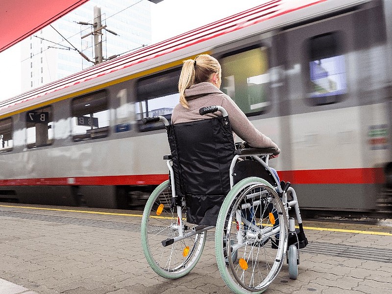 Frau im Rollstuhl am Bahnhof mit vorbeifahrendem Zug