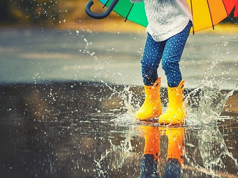 Kind springt mit gelben Gummistiefeln in eine Pfütze