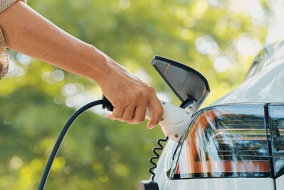Nahaufnahme wie ein Mann eine Ladestation für Elektroautos verwendet in einem Park