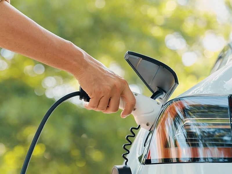 Nahaufnahme wie ein Mann eine Ladestation für Elektroautos verwendet in einem Park