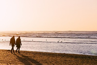 Ein Pärchen läuft Hand in Hand beim Sonnenuntergang am Stand an der Nordsee spazieren