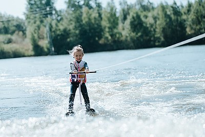 Lächelndes junges Mädchen, das auf einem See wakeboardet und einen sonnigen Tag im Wassersport genießt.