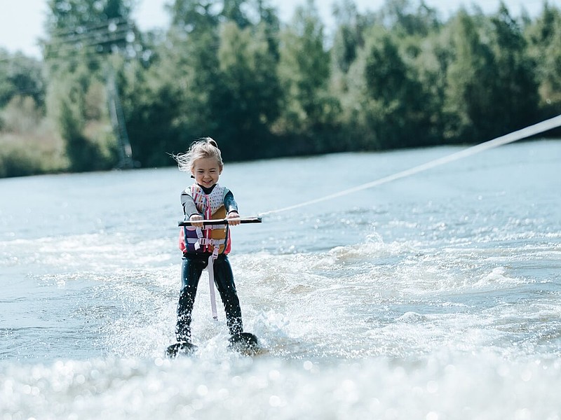 Lächelndes junges Mädchen, das auf einem See wakeboardet und einen sonnigen Tag im Wassersport genießt.