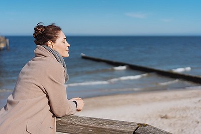 Frau steht an einem Geländer am Meer