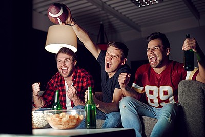3 Männer schaurn auf dem Sofa ein Footballspiel mit passenen Snacks und Getränken