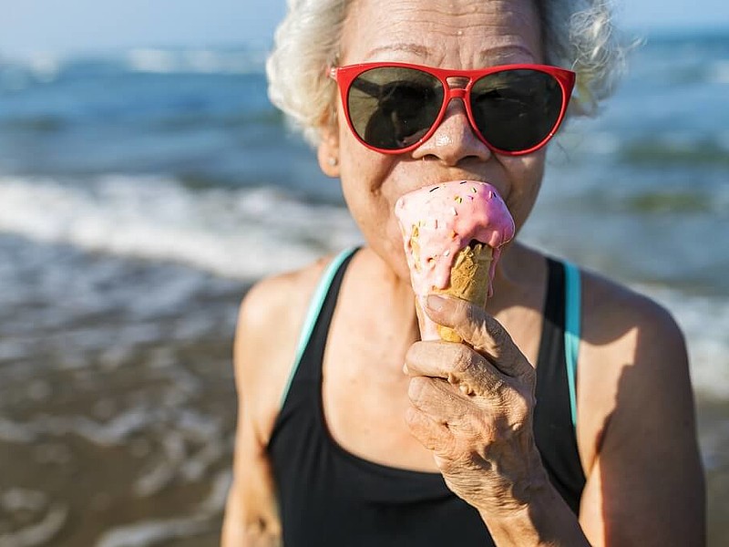 Ältere Frau mit Sonnenbrille isst ein Eis am Strand