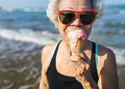Ältere Frau mit Sonnenbrille isst ein Eis am Strand