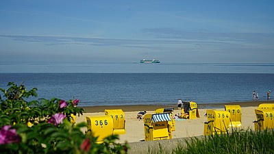 Blick auf den Strand mit gelben Strandkörben und einem Containerschiff im Hintergrund