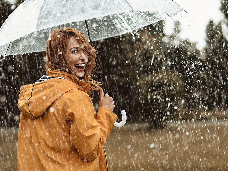 Frau steht mit einer gelben Regenjacke und einem Regenschirm im Regen