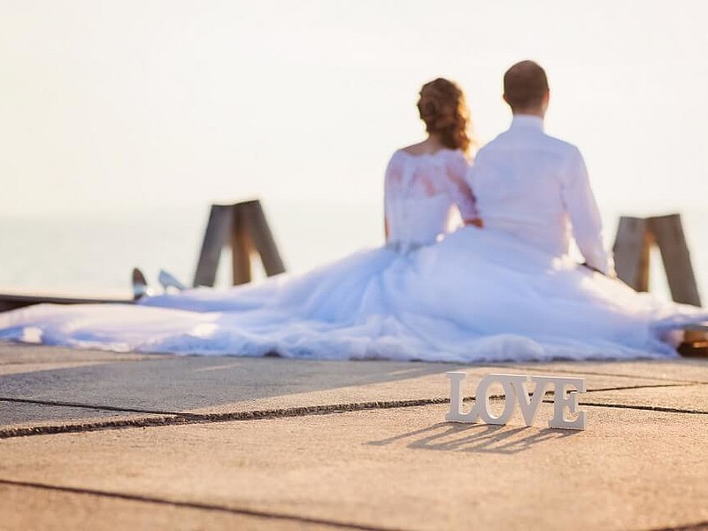 Ein Hochzeitspaar sitzt auf einem Steg und hält die Füße ins Wasser