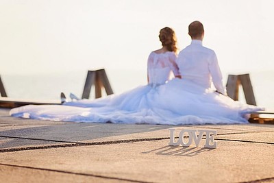 Ein Hochzeitspaar sitzt auf einem Steg und hält die Füße ins Wasser