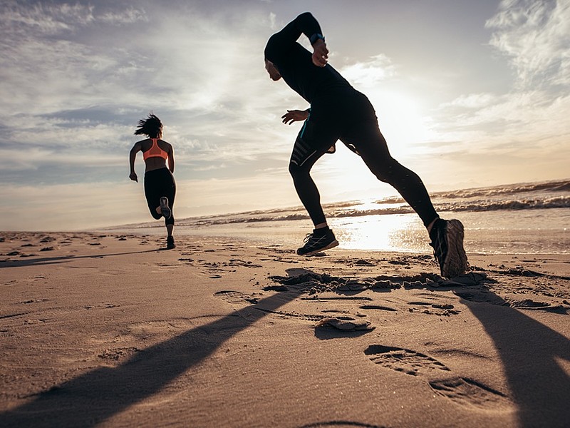 Zwei Personen rennen in Sportkleidung am Strand entlang bei Sonnenuntergang