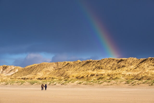 Blick auf einen bunten Regenbogen über den Dünen vom Strand aus