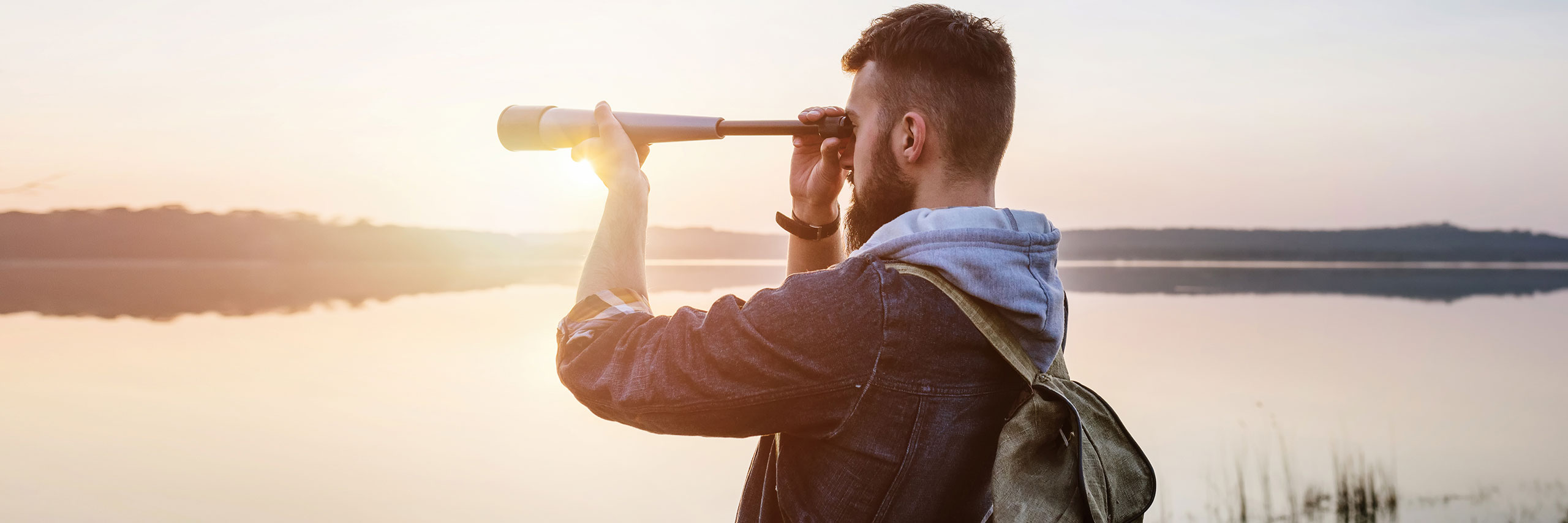 Mann beobachtet mit Fernglas Vögel am Wasser