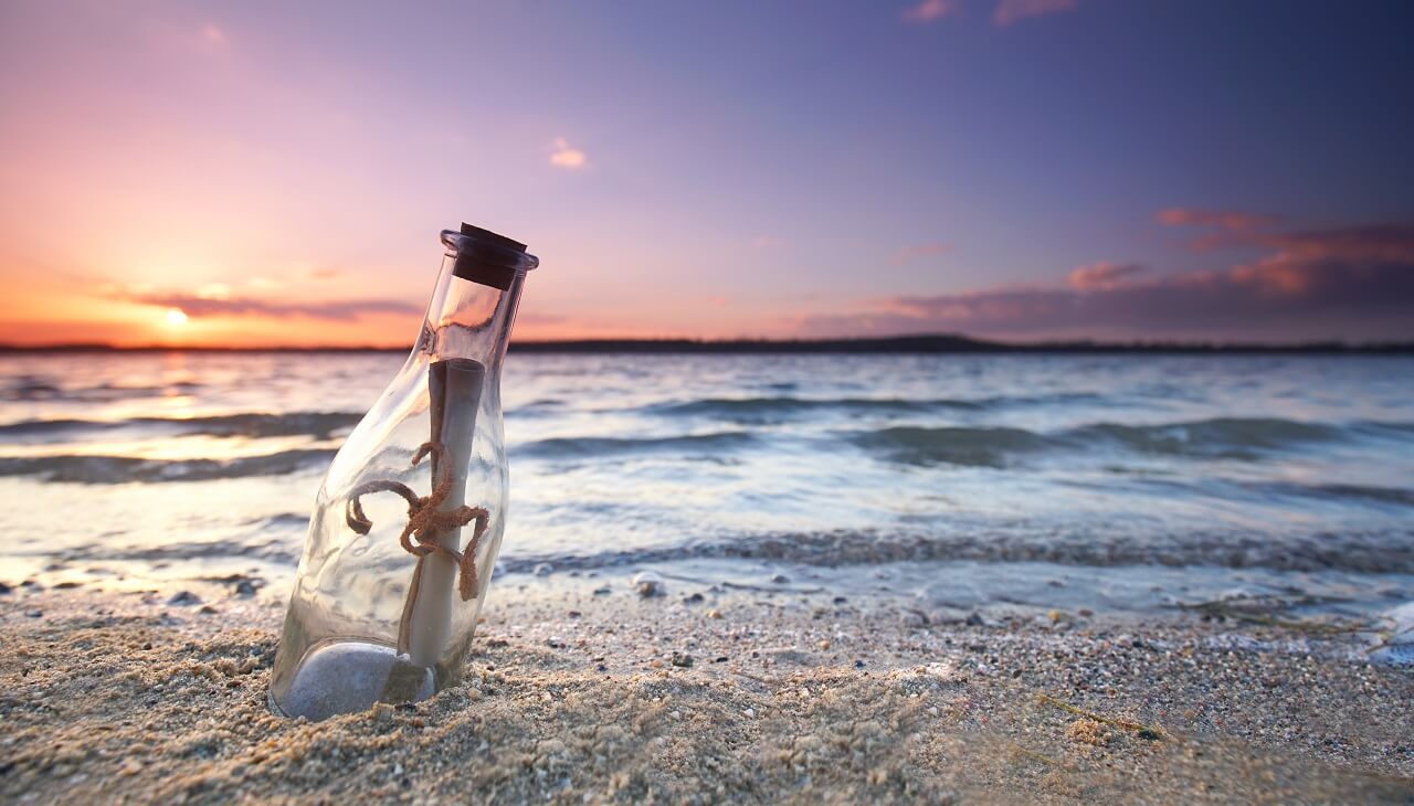 Flaschenpost steht im Sand vor dem Meer mit lila verfärbten Himmel vom Sonnenuntergang