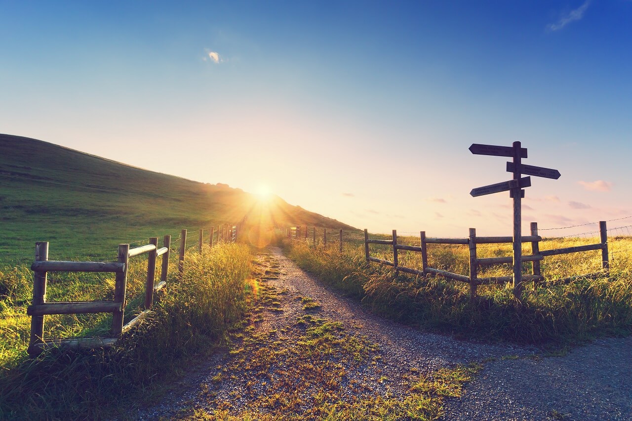 Langer Weg Richtung untergehender Sonne mit einem Wegweiser