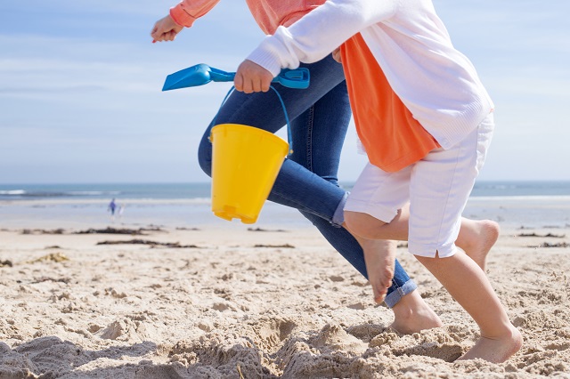 Zwei Personen rennen durch den Sand mit Strandspielzeug in der Hand 
