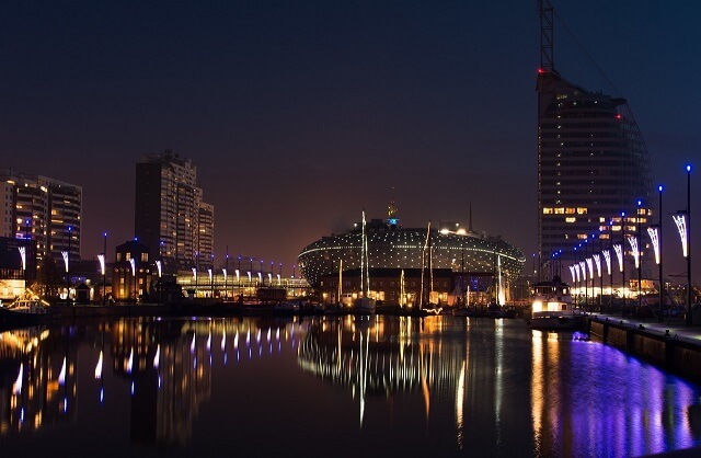 Blick bei Nacht auf das beleuchtete Klimahaus, Sail City Hotel und den Hafen
