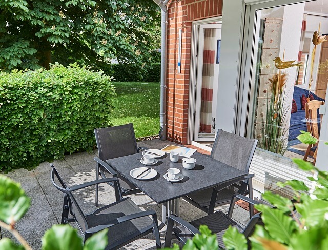 Ein gedeckter Tisch mit Blick in den Gemeinschaftsgarten steht auf der Terrasse einer Ferienwohnung