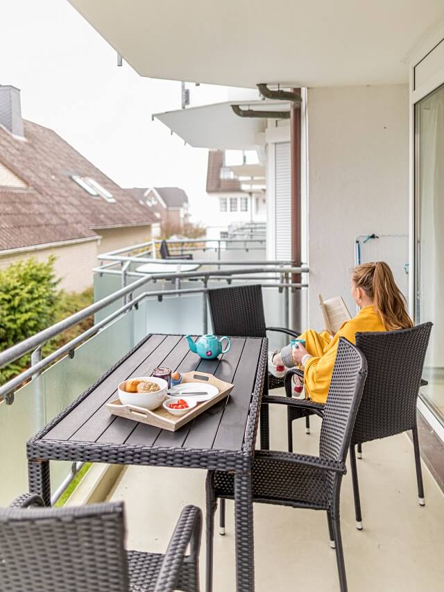 Person sitzt auf dem Balkon und liest ein Buch und trinkt einen Tee