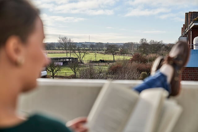 Person ließt ein Buch auf dem Balkon und genießt den Ausblick ins Grüne