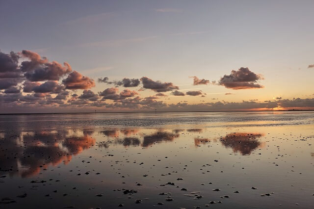 Wolken spiegeln sich auf dem Wattenmeer bei Sonnenuntergang