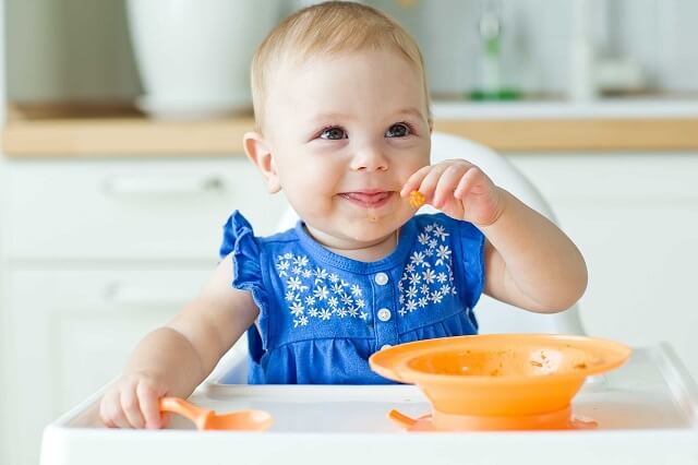 Baby sitzt auf Kinderhochstuhl und isst Brei