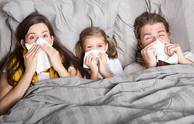 Familie liegt im Bett und hält sich ein Taschentuch vor das Gesicht