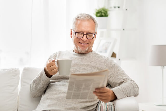 Mann mit Brille trinkt Kaffee und ließt Zeitung
